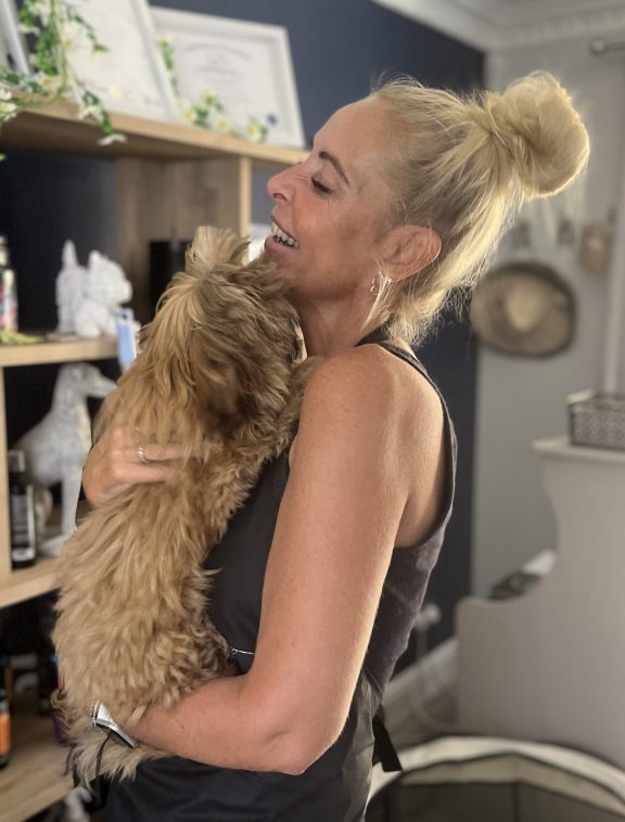 Cheryl, the founder of Daisy Doodle Grooming, holding a small dog, giving them a big cuddle
